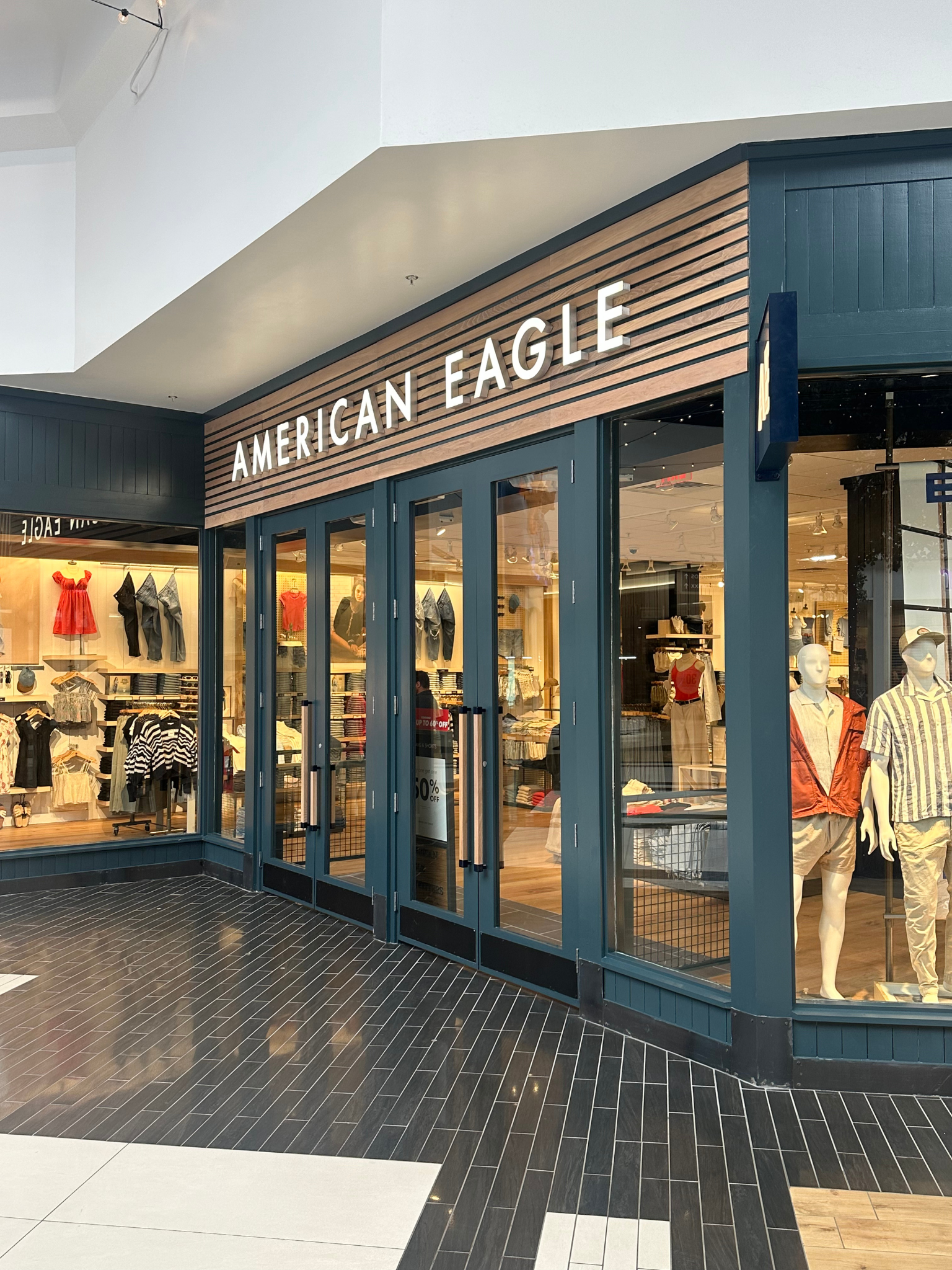 American Eagle store entrance in a mall, with blue doors and bright merchandise displays.
