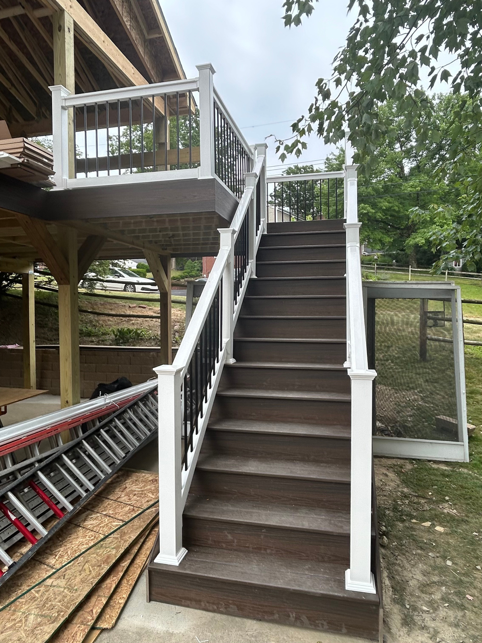 Outdoor staircase with white railings leading to a raised wooden deck beside a house