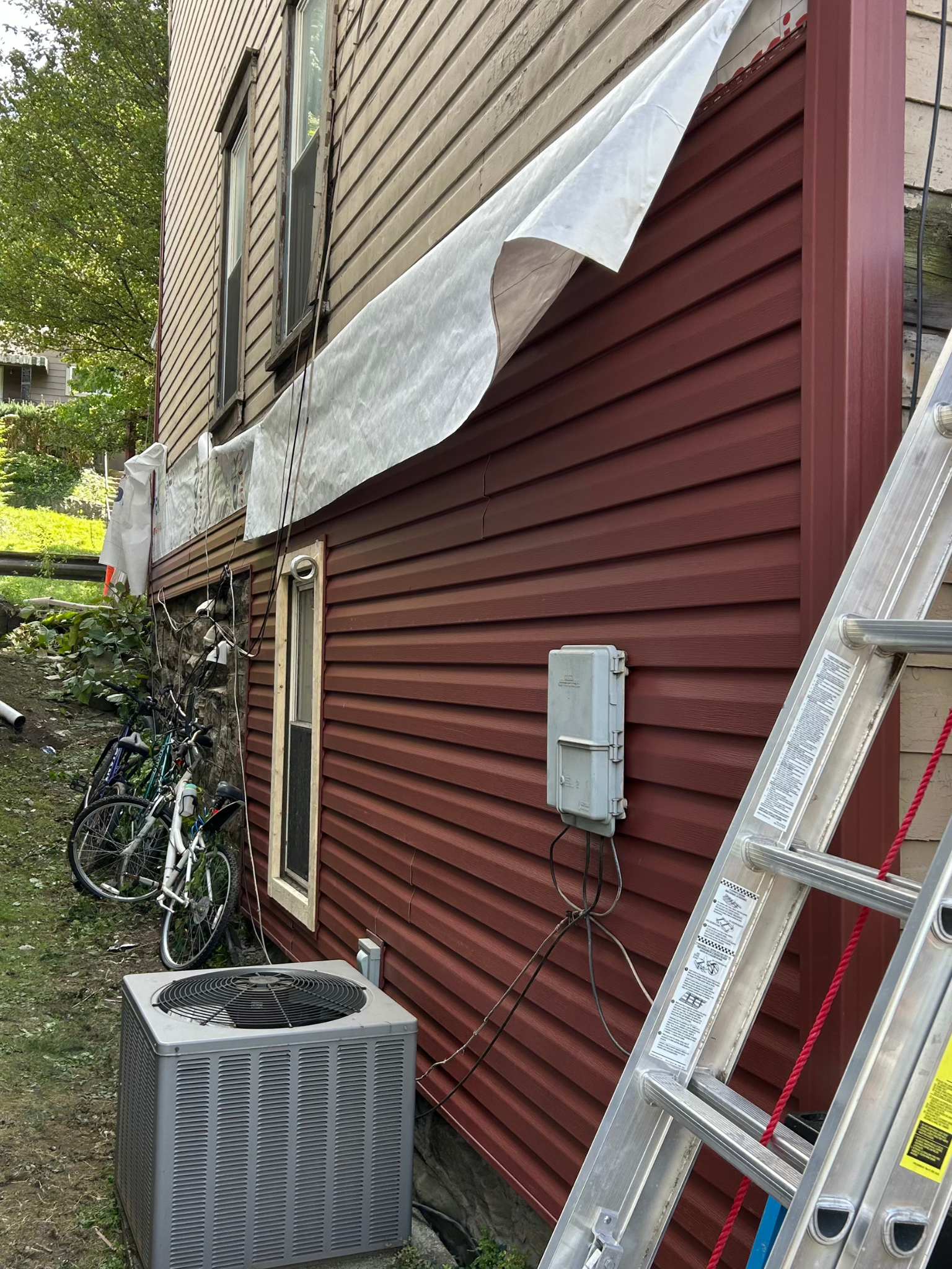 House exterior with red siding, beige upper wall, ladder, AC unit, and a covered section near a garden path