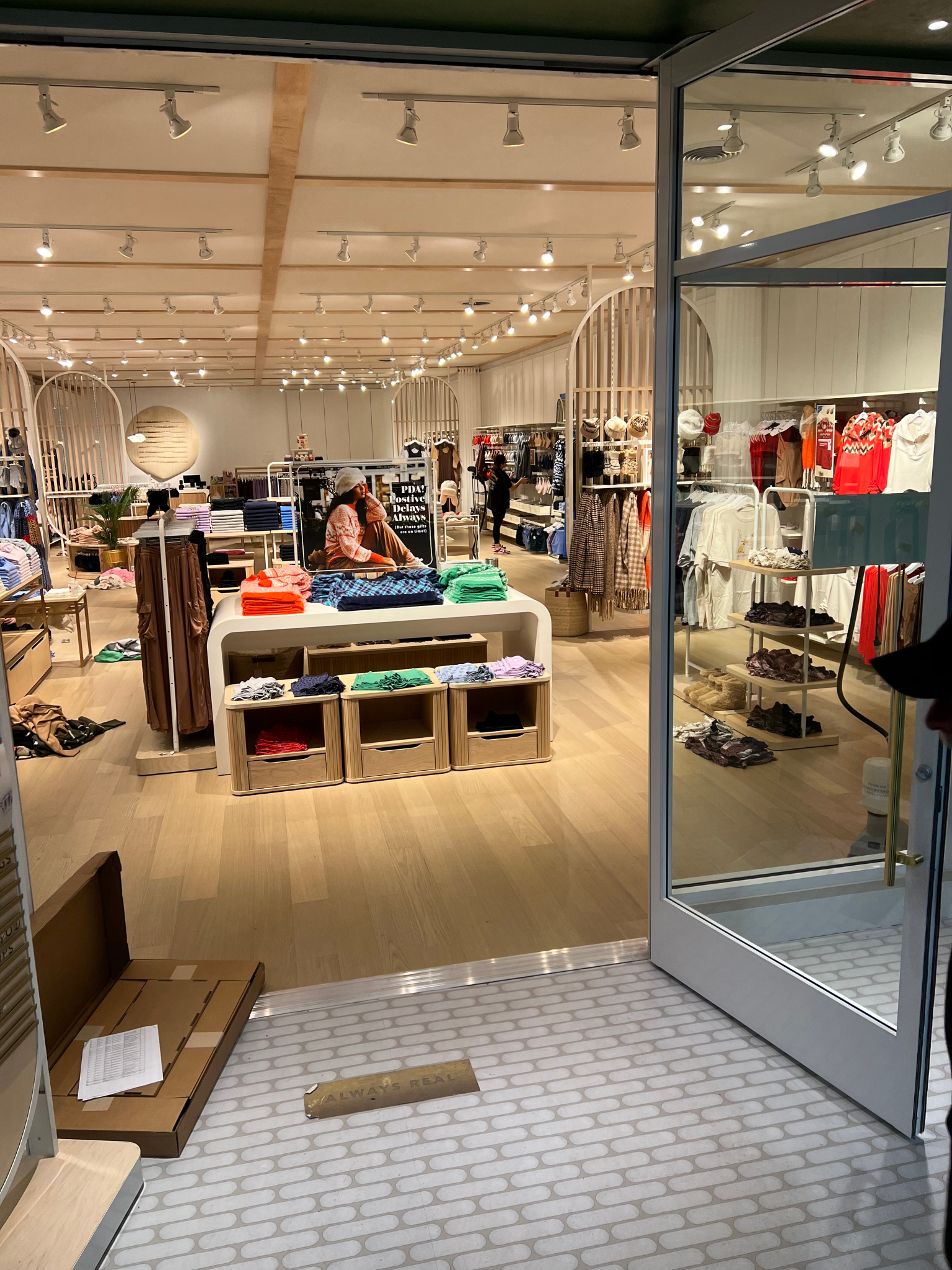 Clothing store entrance with racks of clothes, a display table, and warm string lights inside.