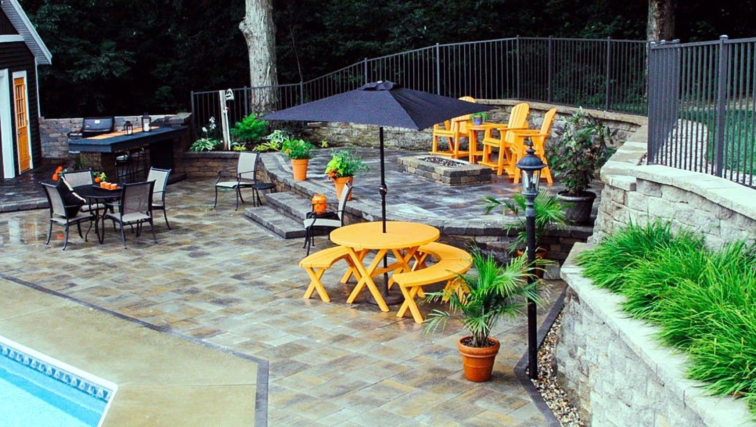 Outdoor patio with orange furniture, black umbrella, stone retaining walls, and a pool.