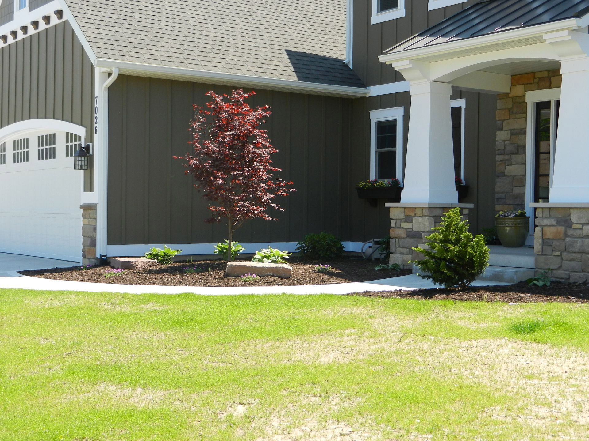 Exterior of a house with a red tree and green lawn. Garage door on the left, stone columns on the right.