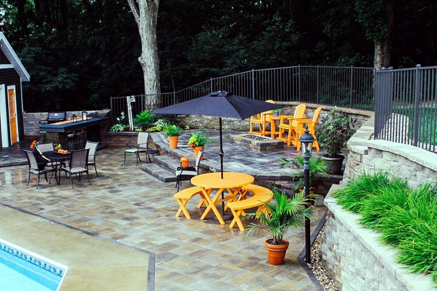 Patio with yellow furniture, a black umbrella, and stone retaining walls, near a pool.