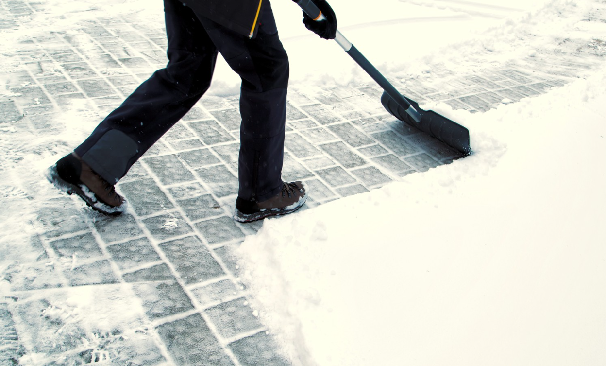 A person is shoveling snow from a sidewalk with a shovel