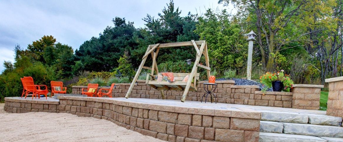 A backyard with a stone wall, chairs, and a swing