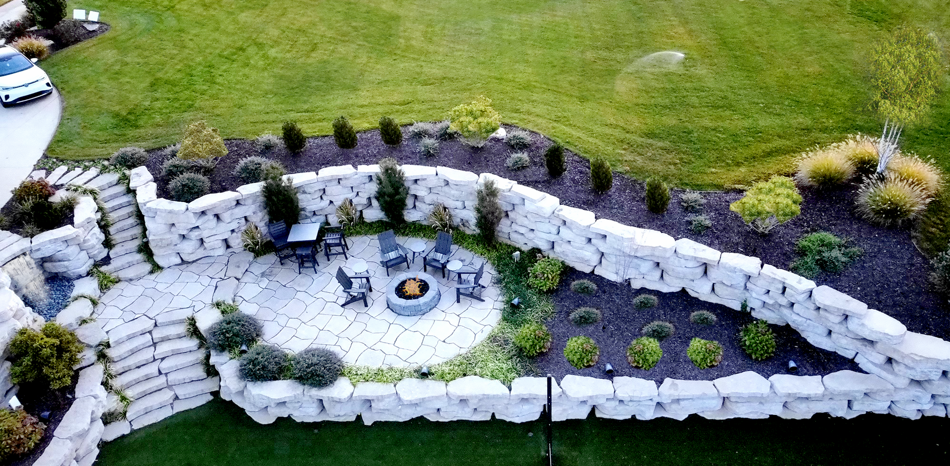 An aerial view of a backyard with a fire pit and a stone wall.