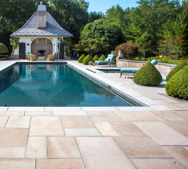 Stone patio surrounds a pool with a gazebo, manicured shrubs, and lounge chairs in a sunny outdoor setting.