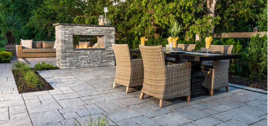 Outdoor patio with stone fireplace, dining table with wicker chairs, and a sofa.
