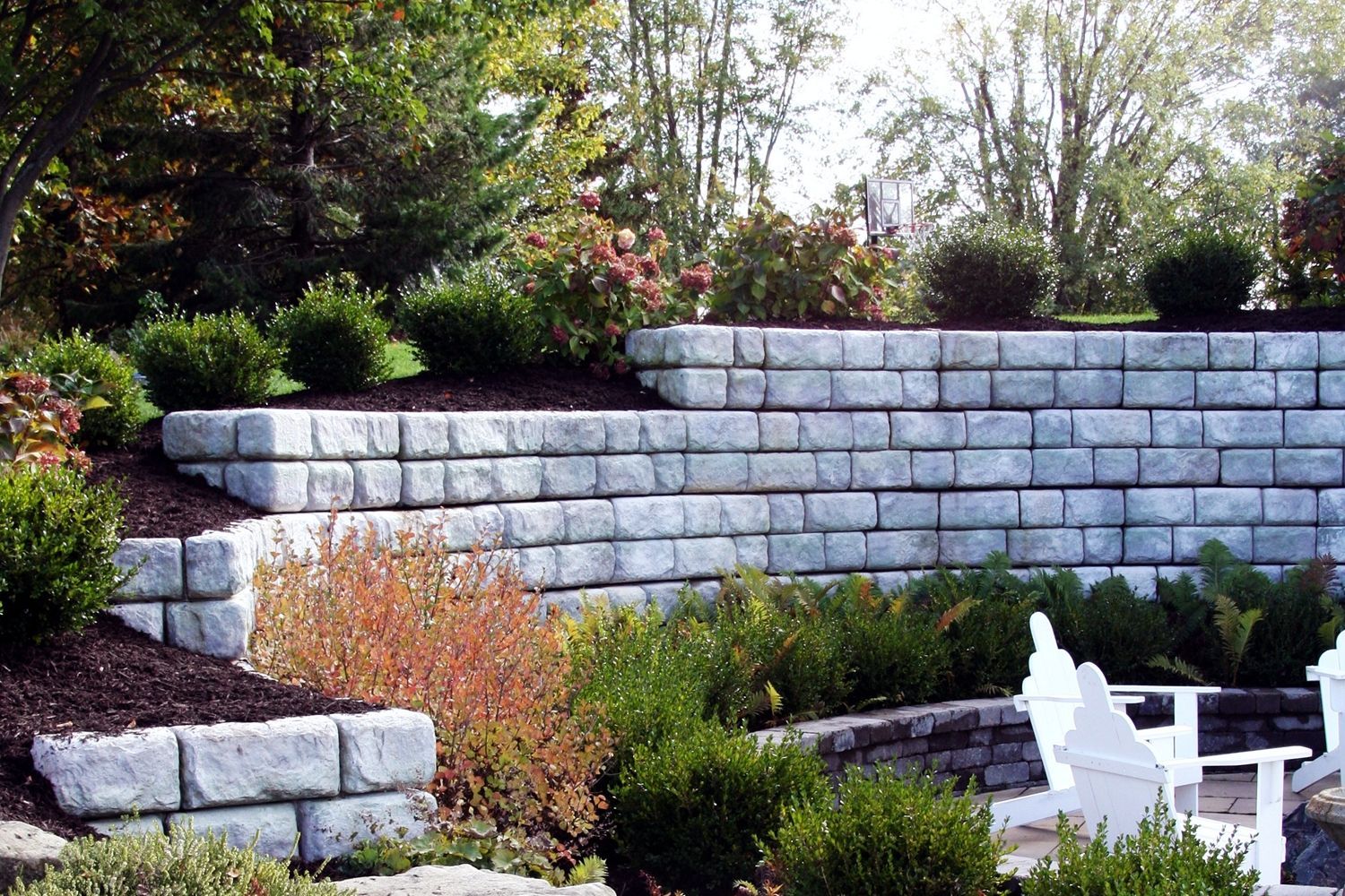 A stone wall in a garden with a few chairs in front of it.