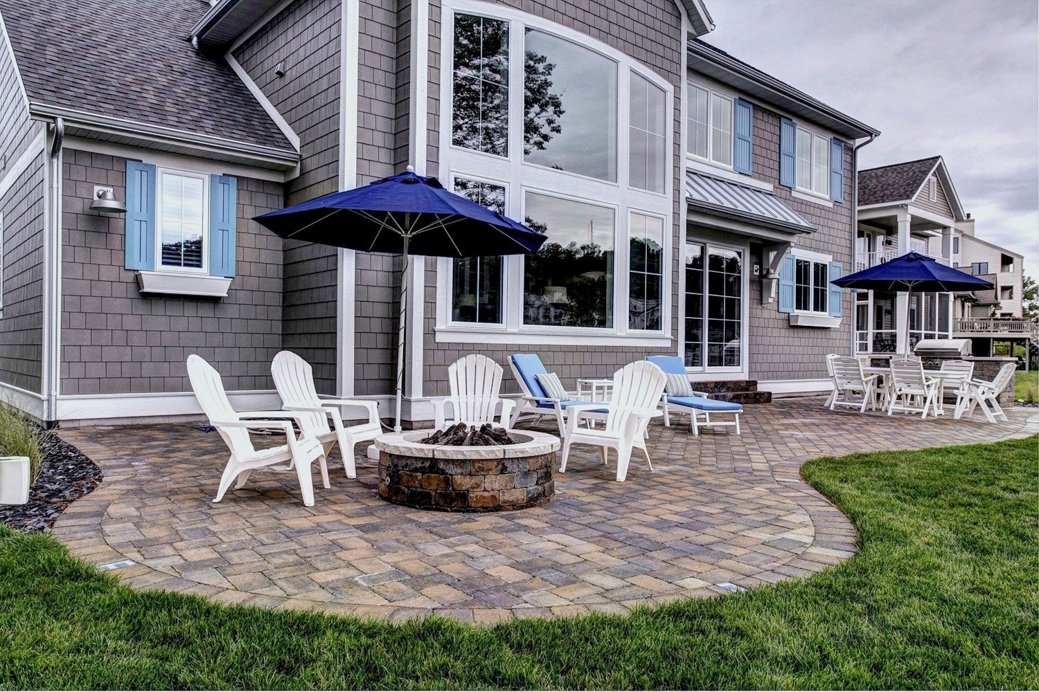 A large house with a patio with chairs and umbrellas and a fire pit.
