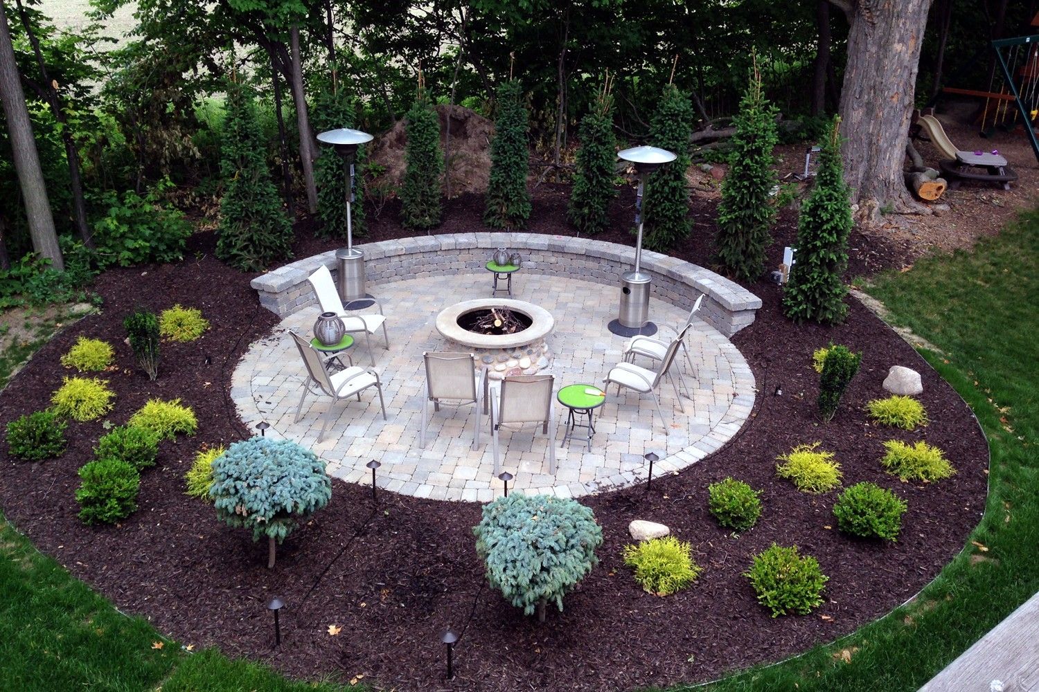There is a fire pit in the middle of the patio surrounded by plants.