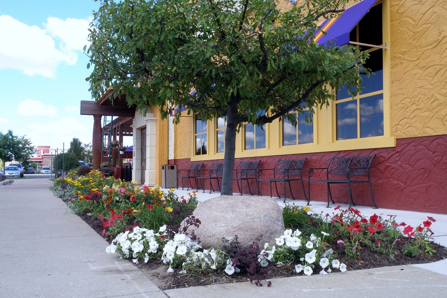A yellow building with a purple awning and flowers in front of it