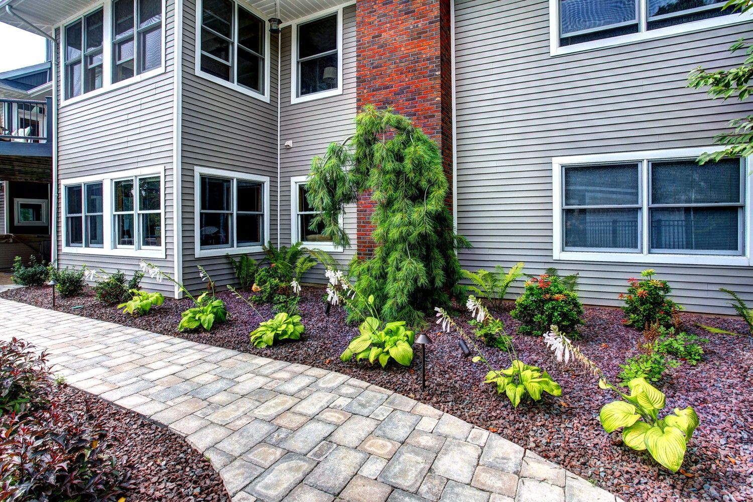 A brick walkway leading to a large house with lots of windows.