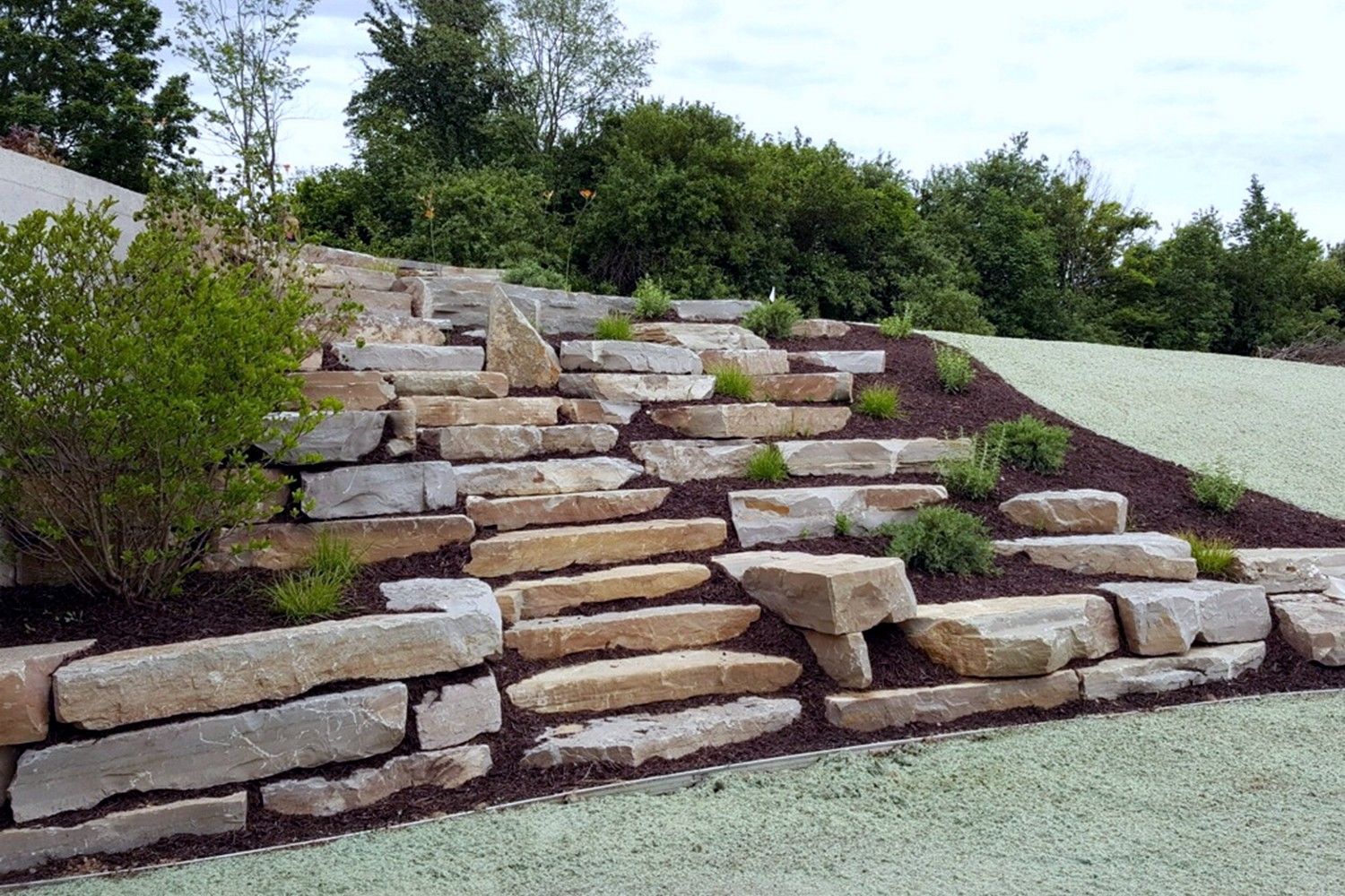 A stone wall with steps leading up to a grassy hillside.