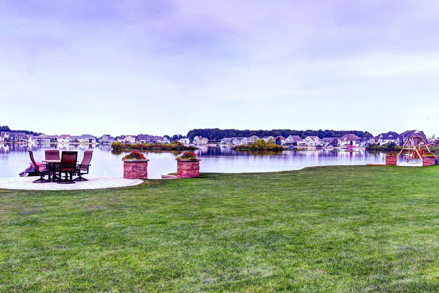 A lawn with a table and chairs next to a lake.