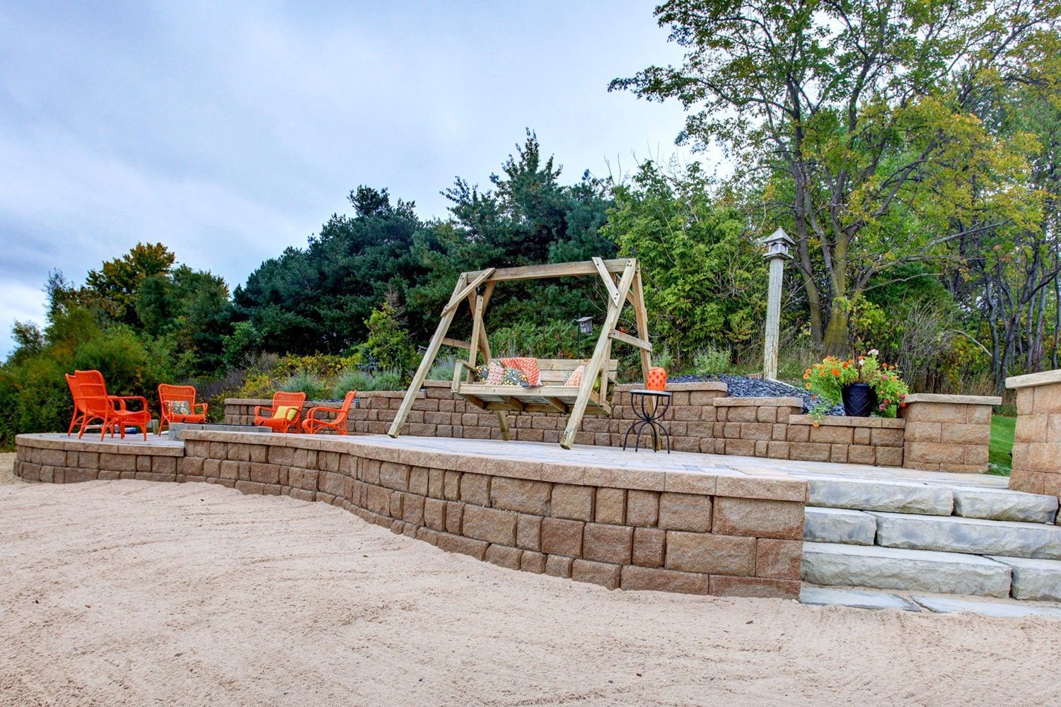 A wooden swing is sitting on top of a patio next to a stone wall.