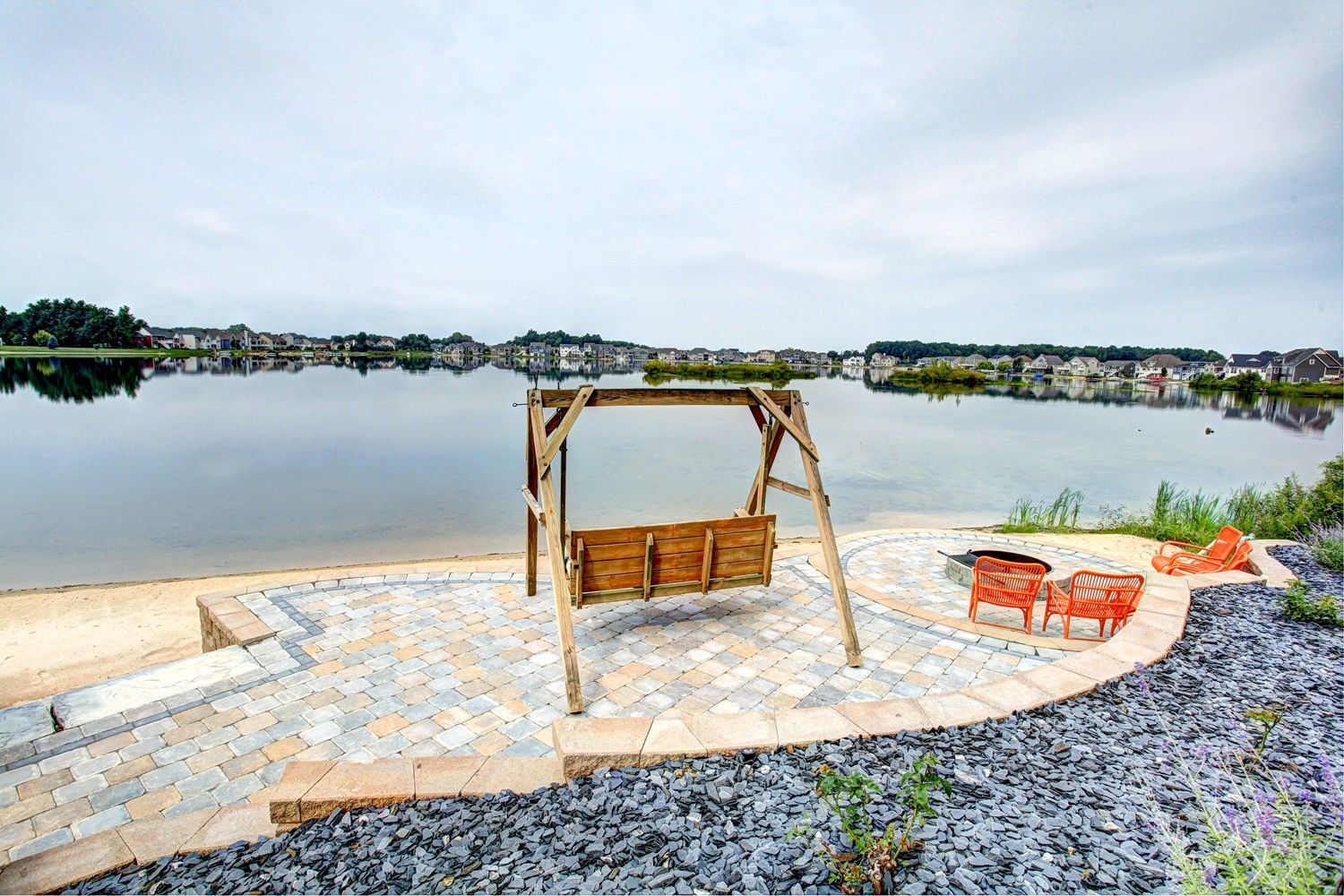 A wooden swing is sitting on a patio next to a lake.