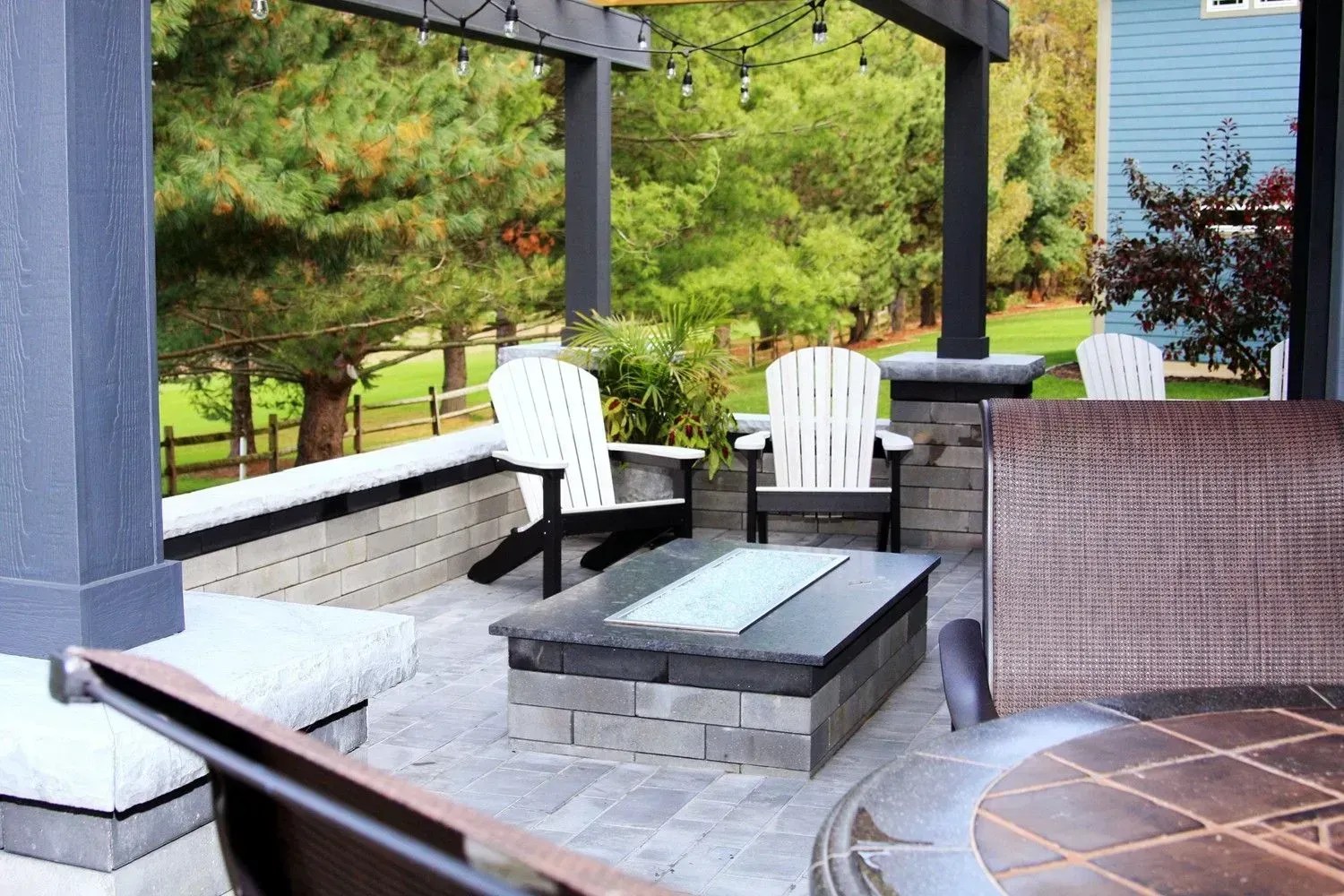 A patio with a fire pit and chairs under a pergola