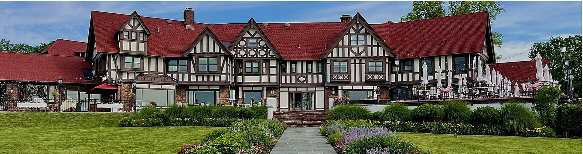 Tudor-style mansion with red roofs and timber framing behind a garden path and green lawn