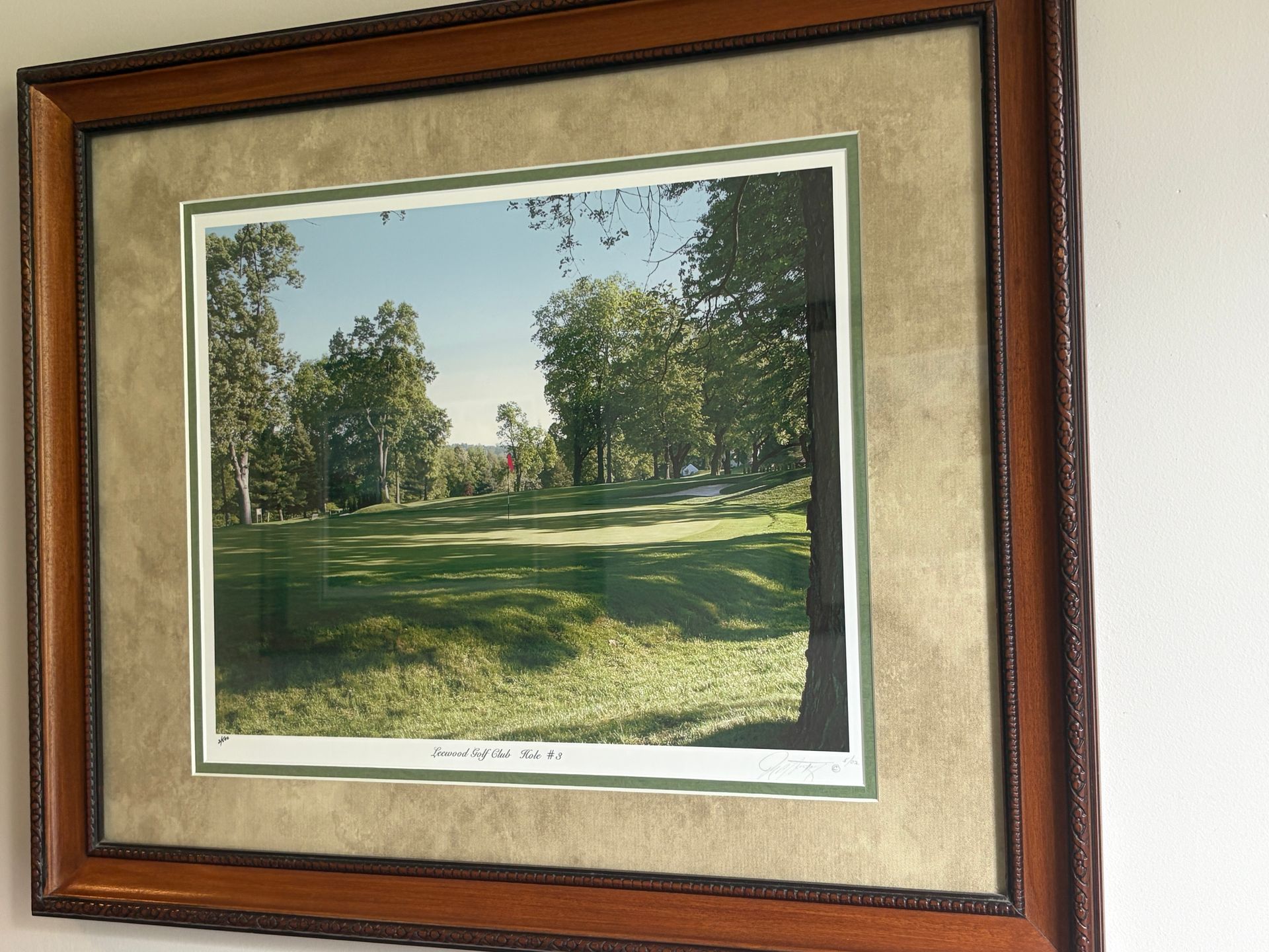 Framed landscape print of a sunlit golf course with trees and green grass on a beige wall