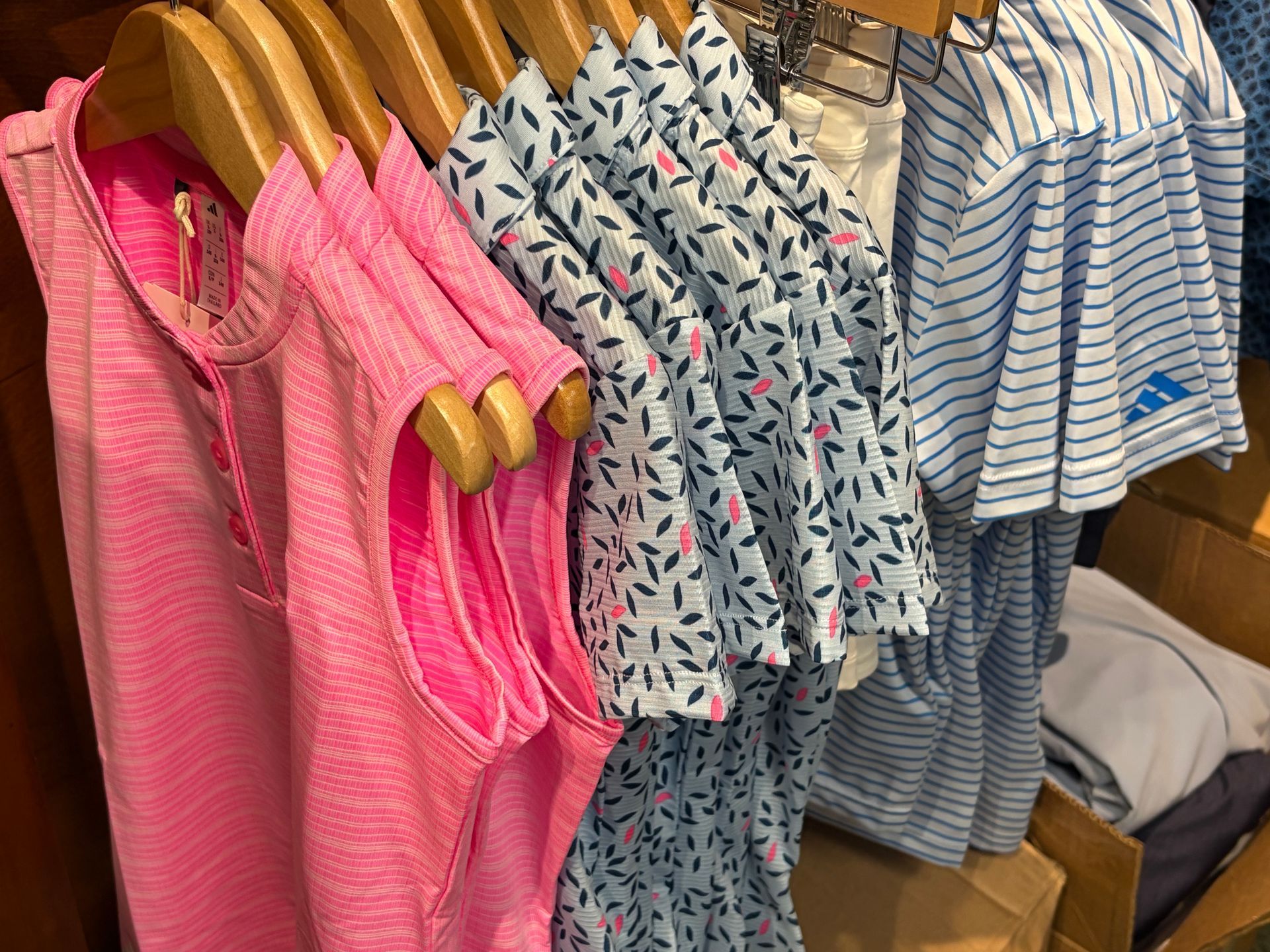 Bright pink and striped children’s shirts hanging on wooden hangers in a clothing store display