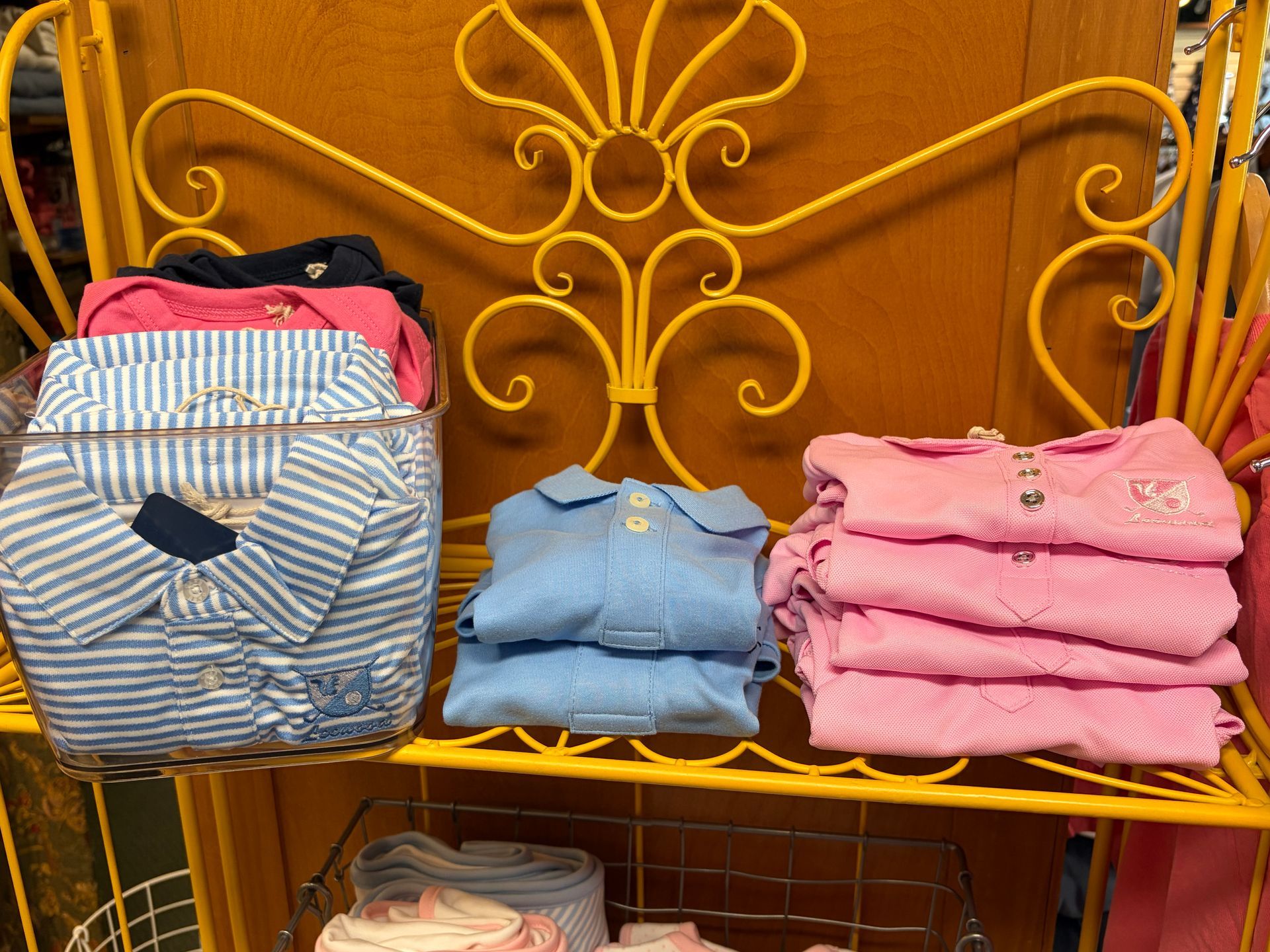 Colorful folded shirts and a striped tote displayed on a yellow metal shelf.