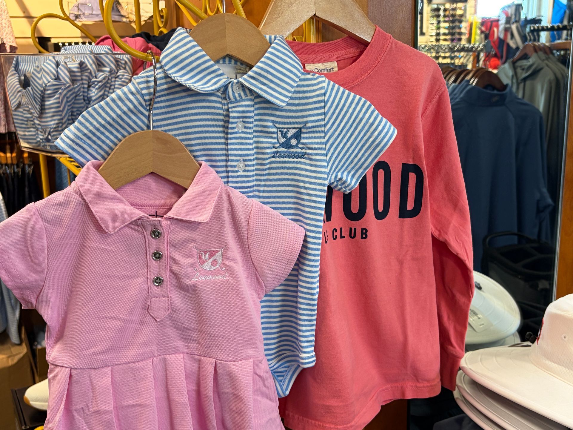 Children’s striped and pink dresses and a pink “club” T-shirt on hangers in a clothing store