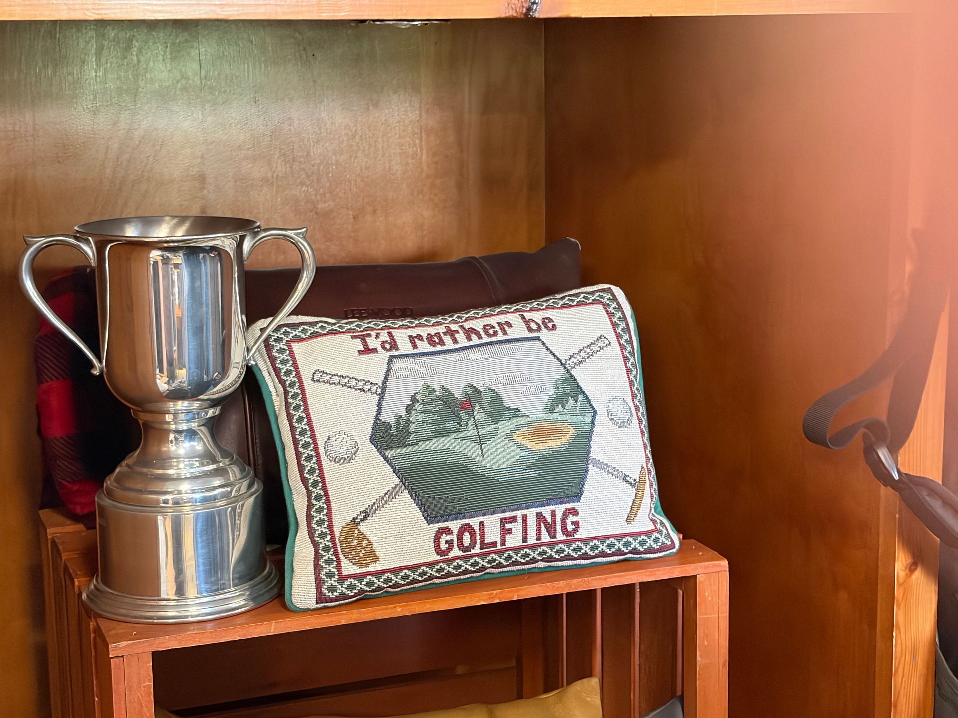 Silver trophy beside a stitched golf-themed bag on a wooden shelf.
