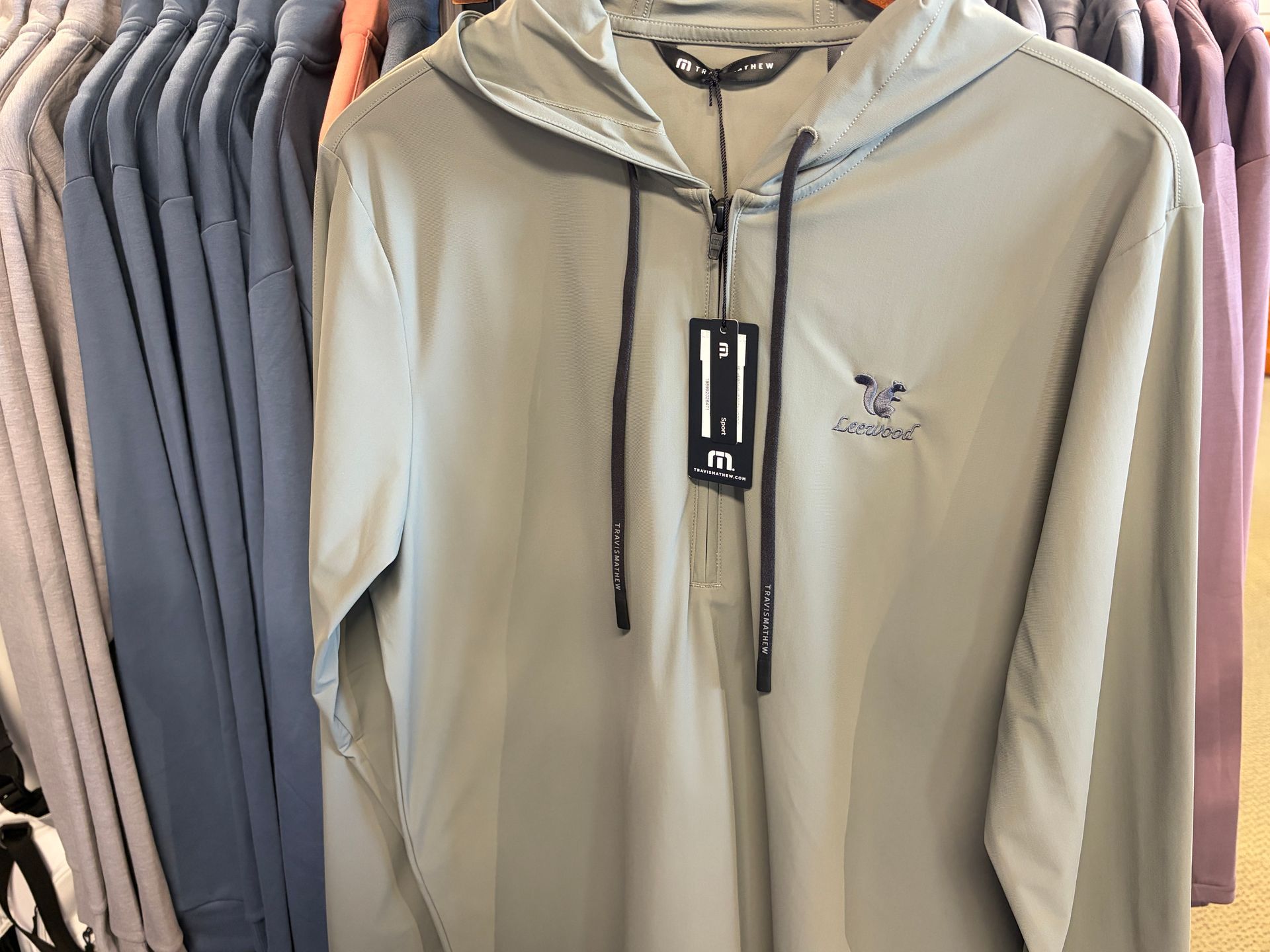 Beige zip-up hoodie with black drawstrings hanging on a clothing rack