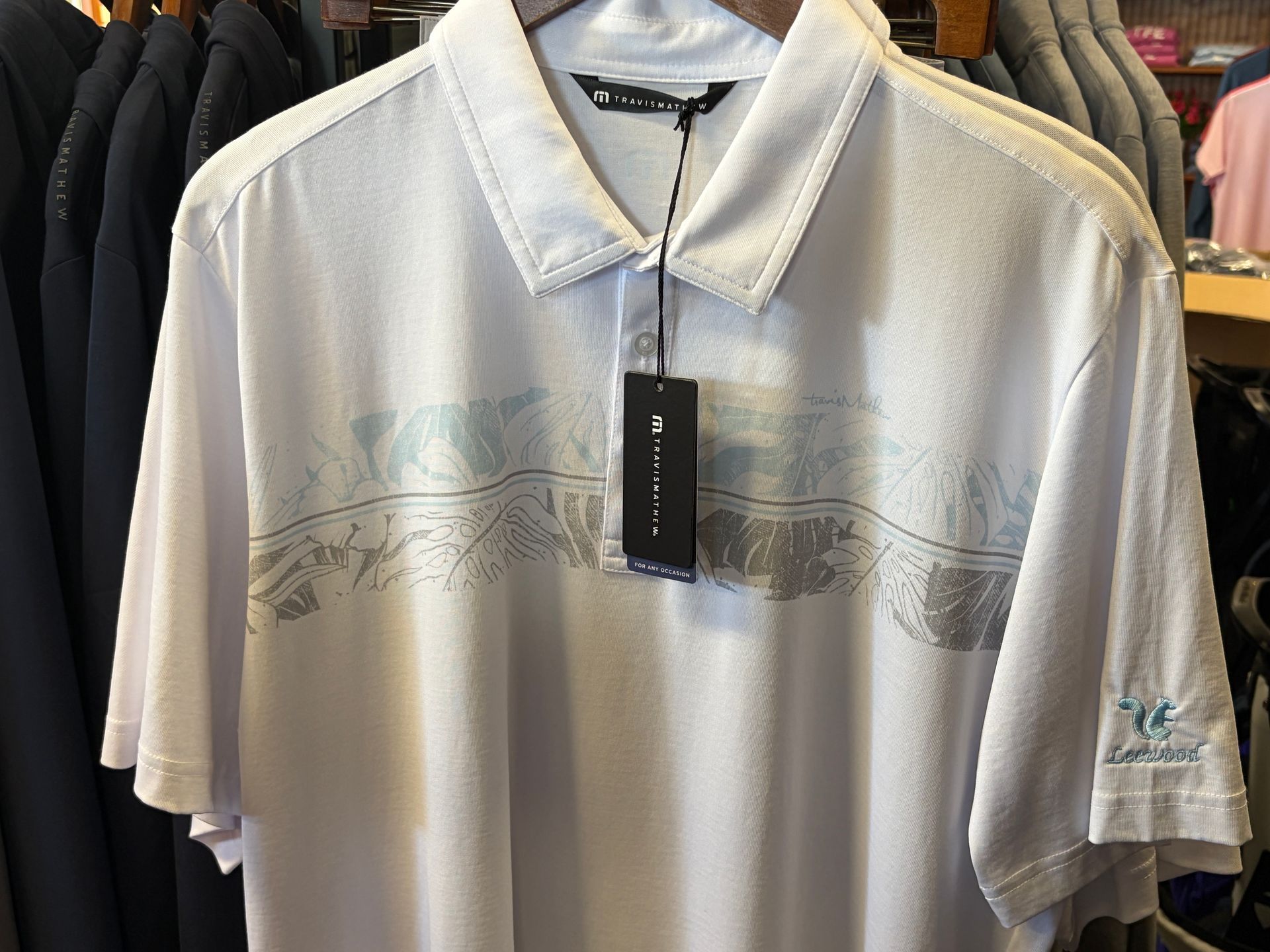 White short-sleeve polo shirt with subtle palm tree print hanging on a store rack