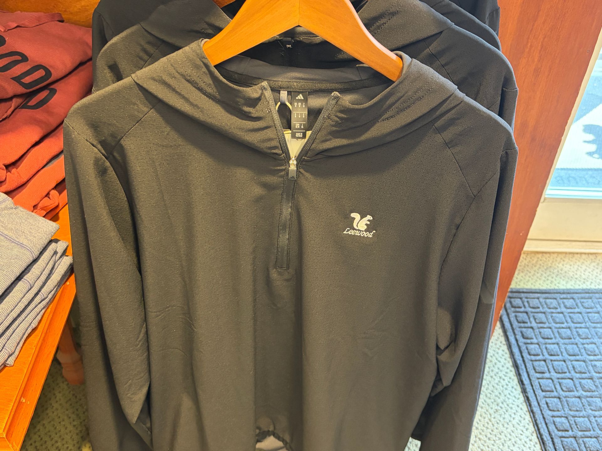 Dark gray zip-up jacket on an orange hanger, displayed beside folded clothes on a shelf.