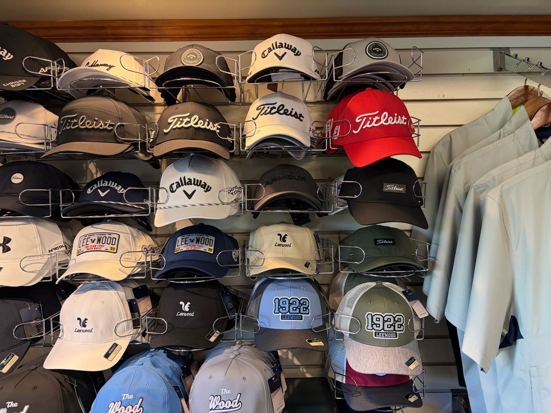 Wall of assorted golf caps and visors in a store display, with white shirts hanging at right