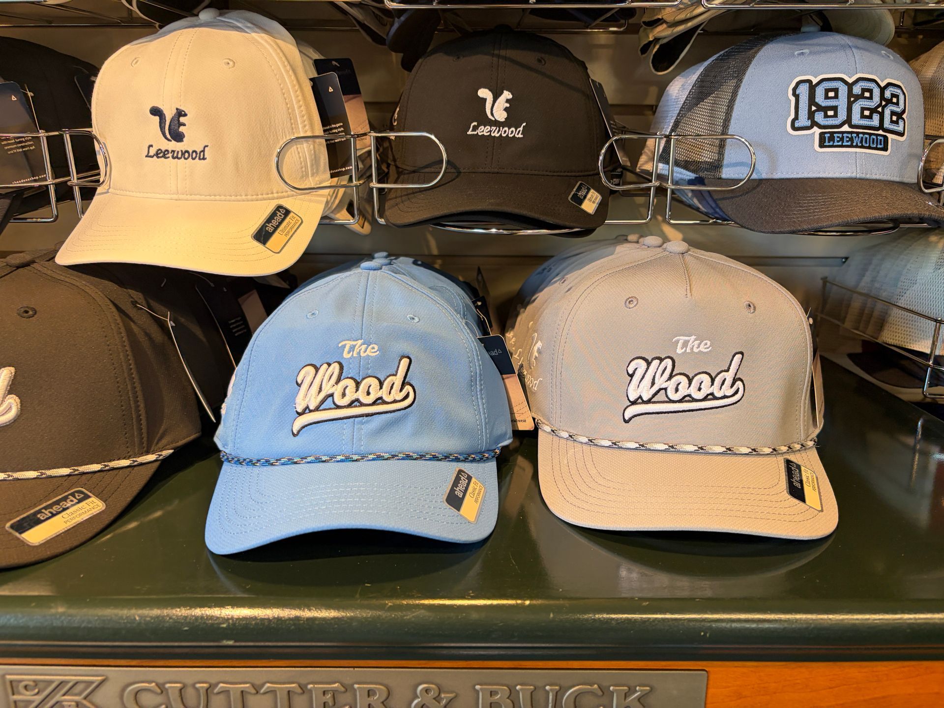 Display of baseball caps on a shelf, including tan, black, blue, and beige hats with embroidered logos.
