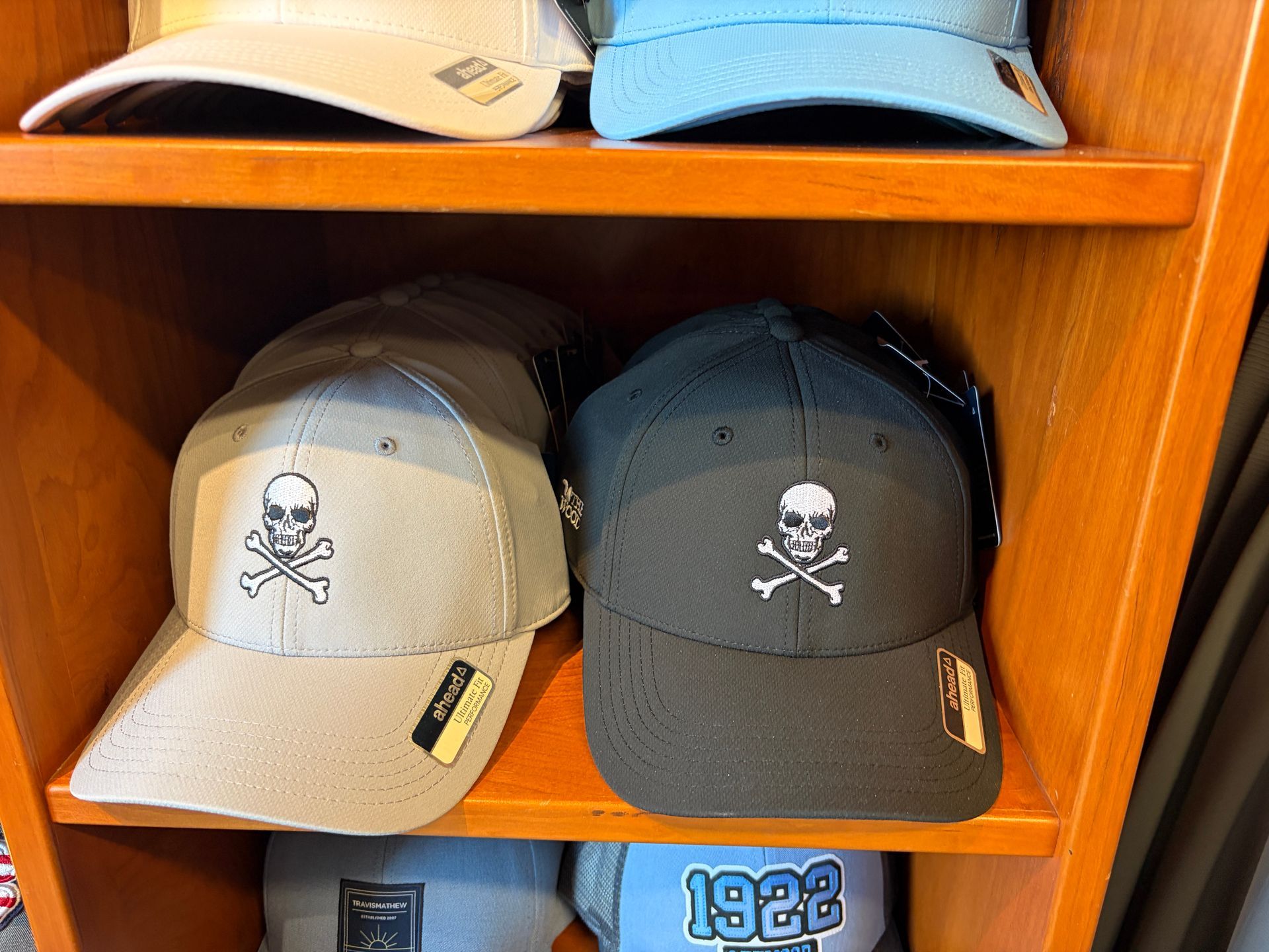 Baseball caps with skull logo on a wooden shelf, in beige, gray, and blue.
