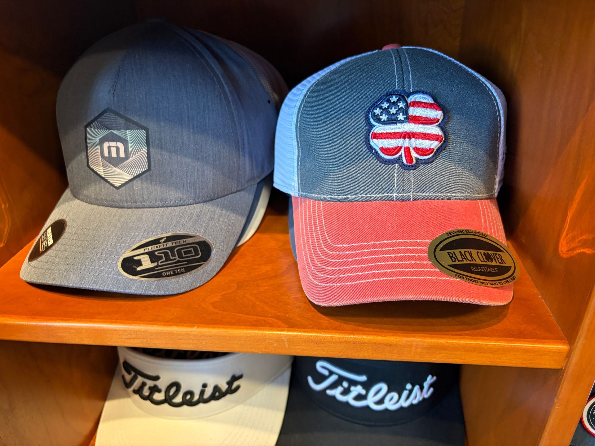 Two baseball caps on a wooden shelf, one gray and one blue with a U.S. flag design.