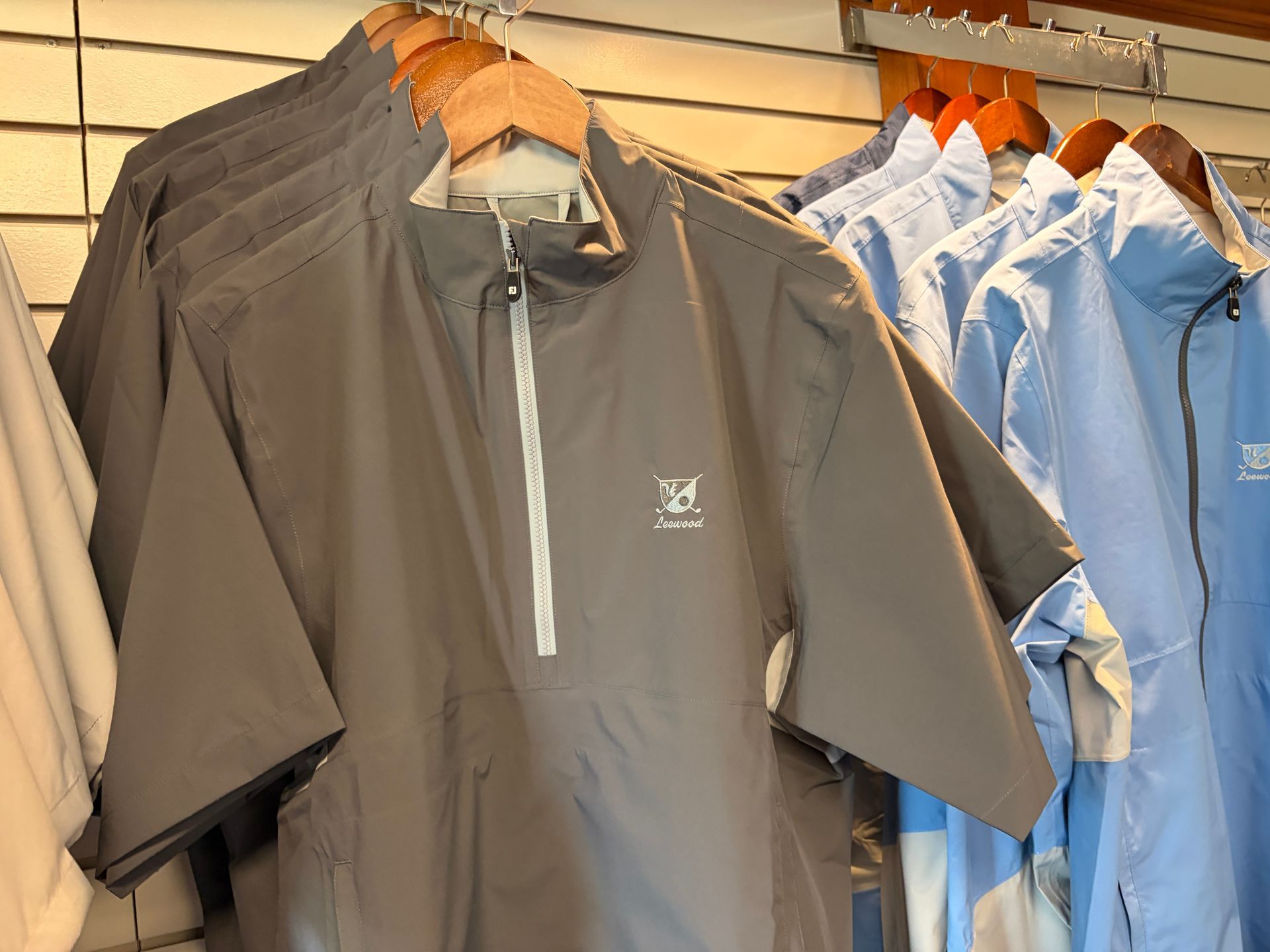 Hanging zip-up shirts in gray and blue on wooden hangers in a retail store.