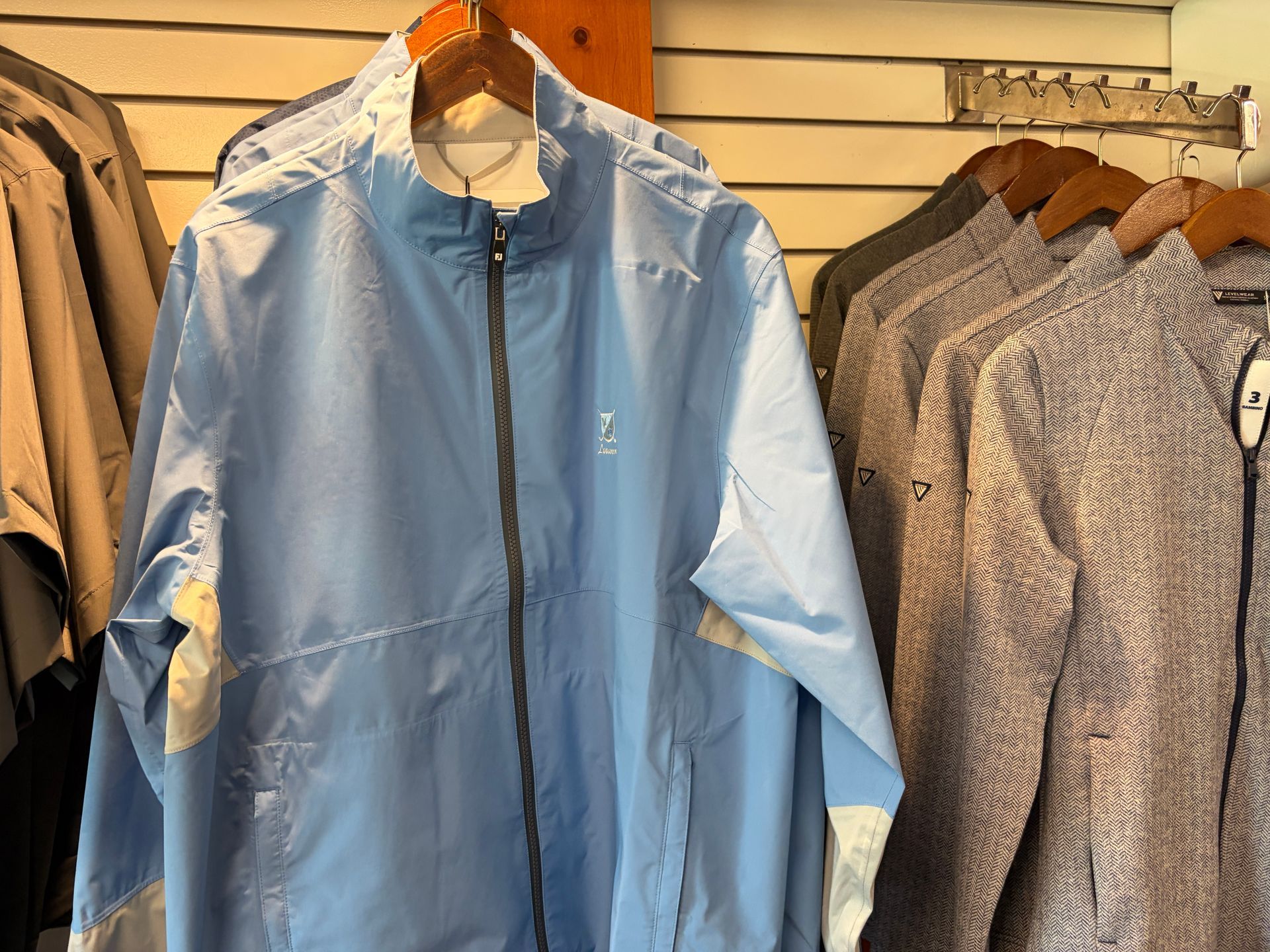 Light blue zip-up jacket hanging in a clothing store next to patterned shirts