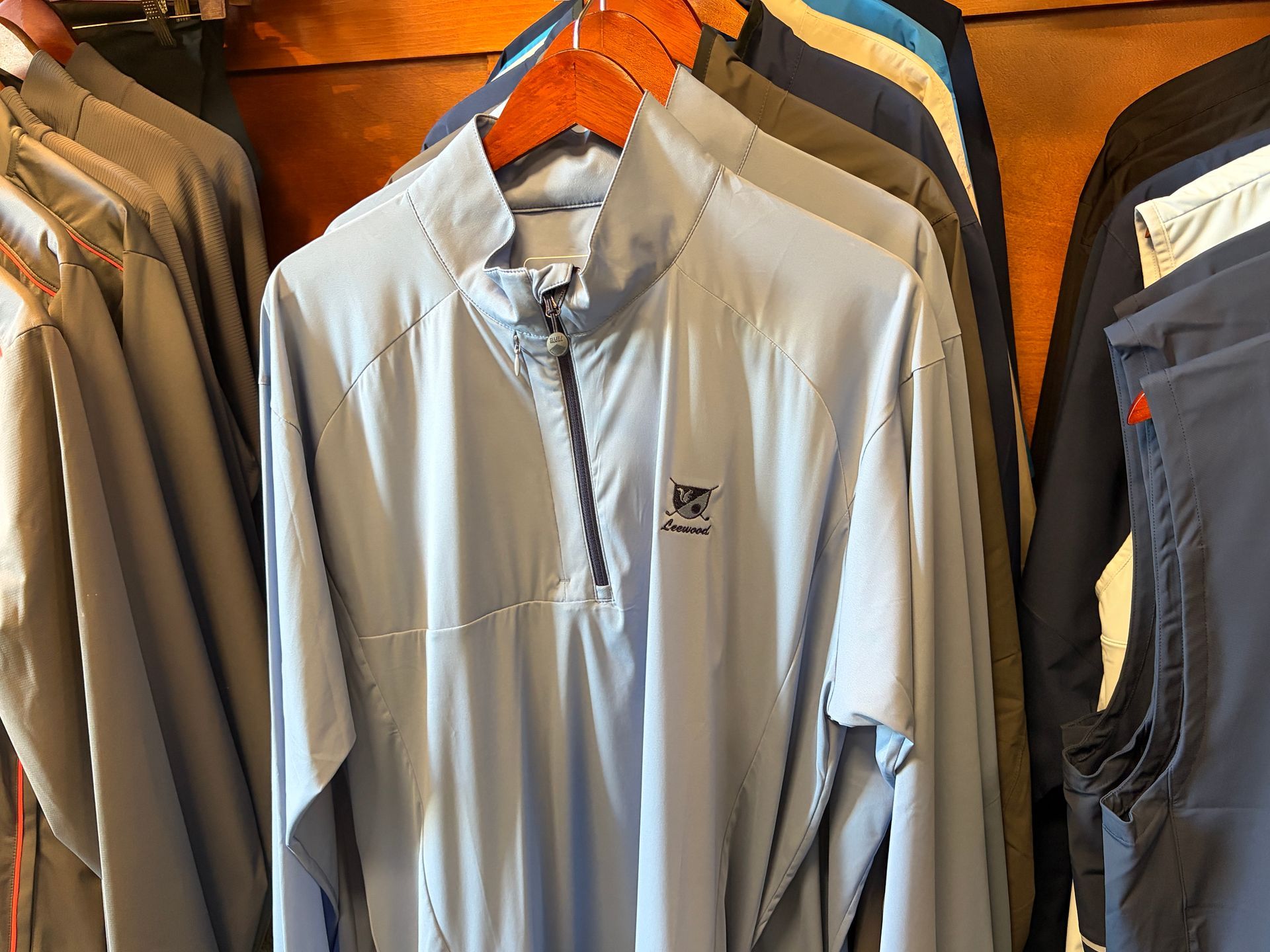 Light gray quarter-zip jacket hanging among other jackets on wooden hangers in a store.