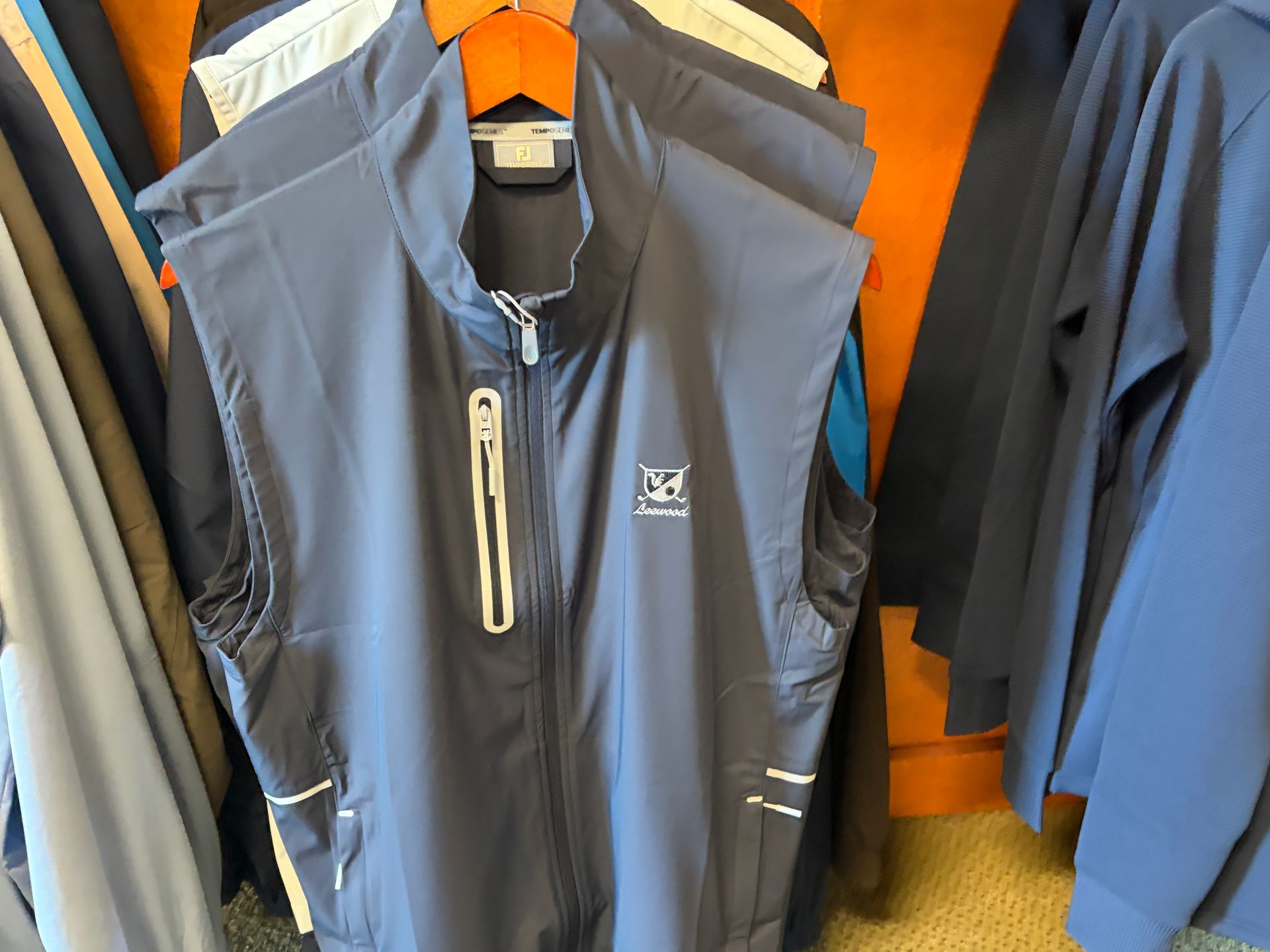 Blue sleeveless zip-up vest hanging among other jackets on a clothing rack