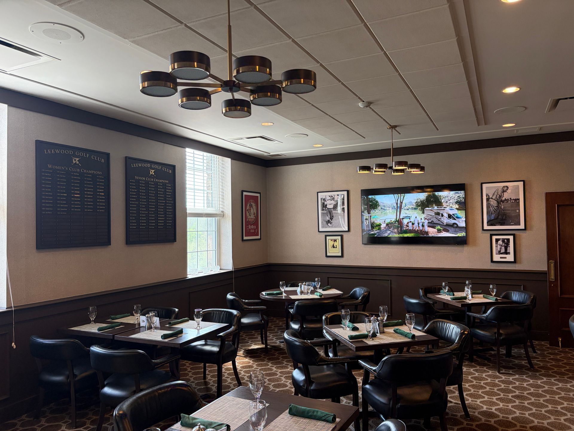 Empty sports bar dining area with dark tables, black booths, wall TVs, and warm ceiling lights