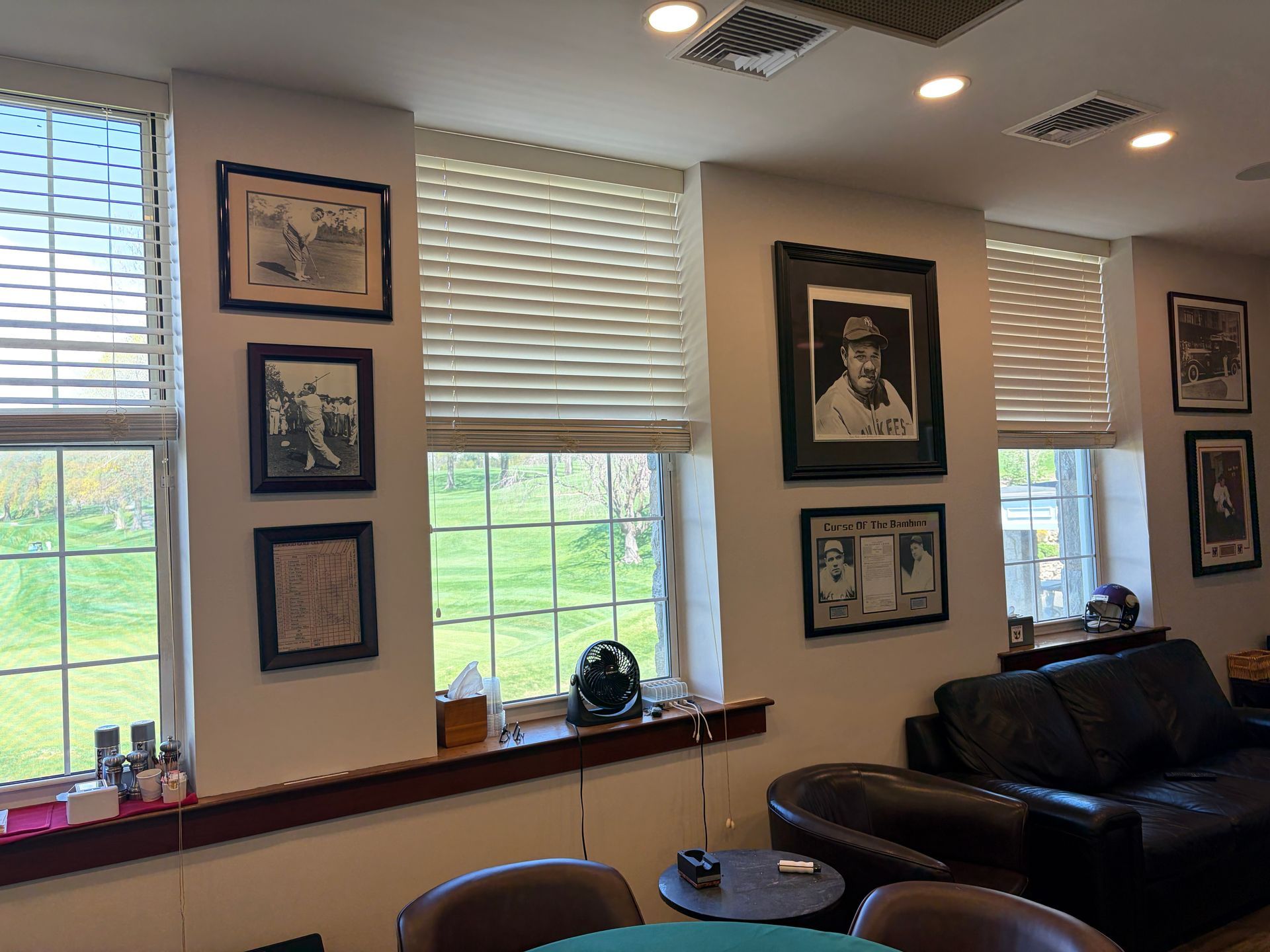 Living room with framed wall art, windows with blinds, and a black leather sofa.
