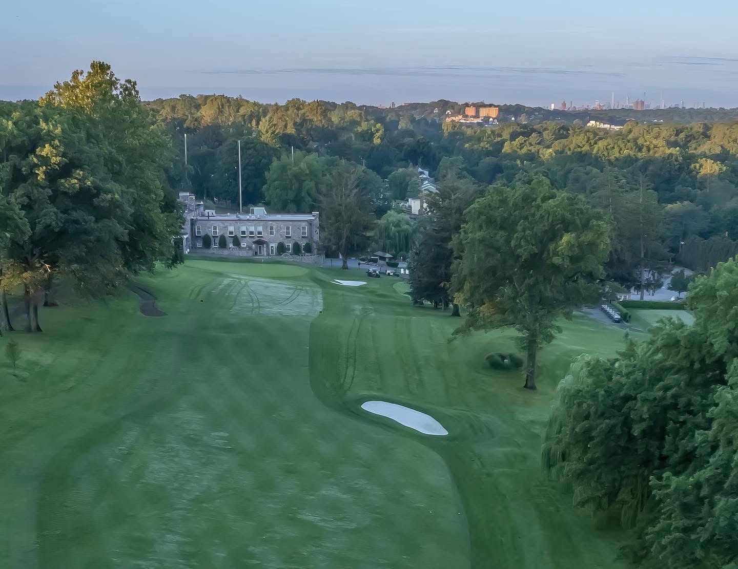 Golf ball on a bright green fairway at sunset with trees and a sand trap in the background.