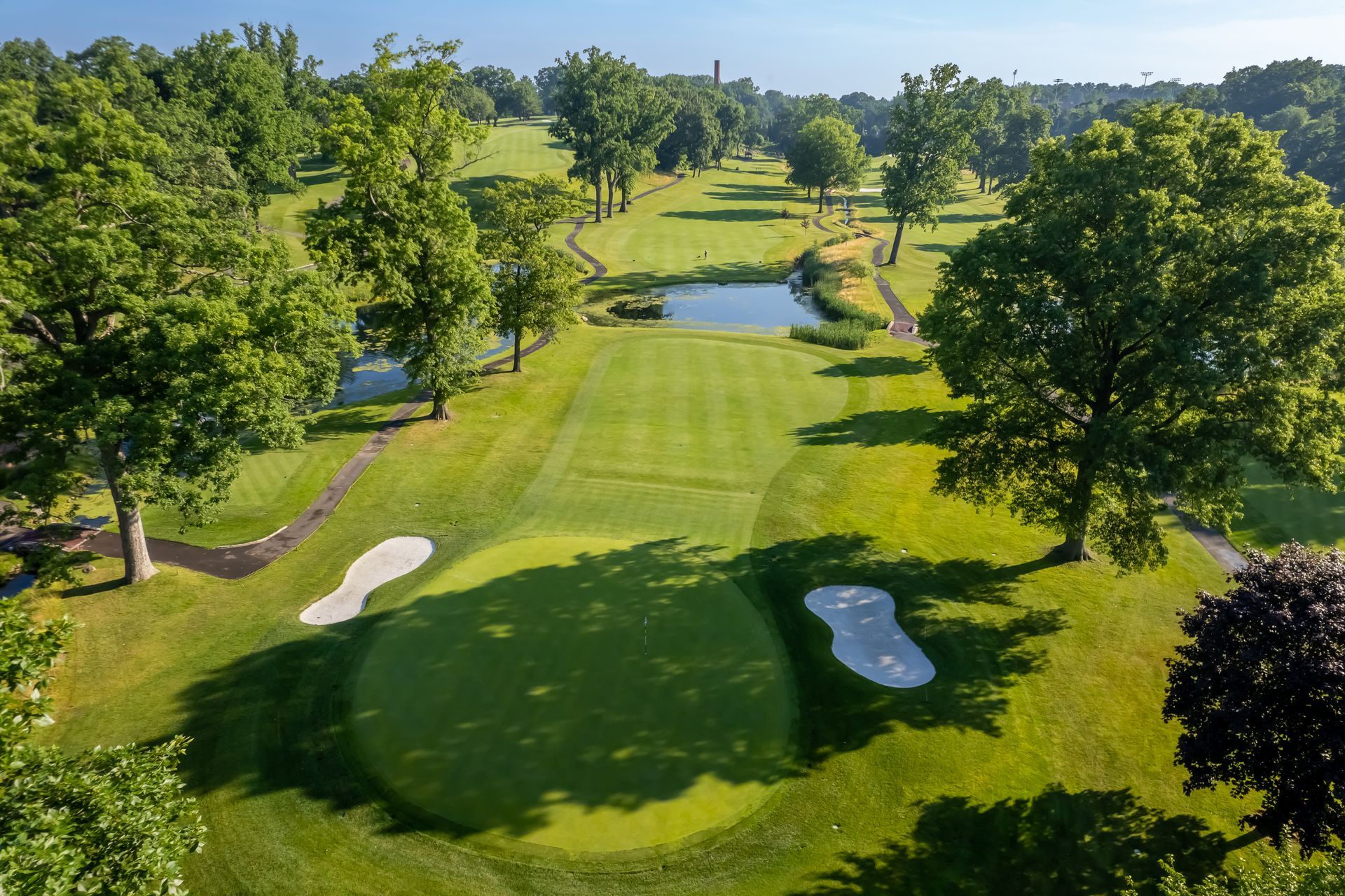Aerial view of a green golf course with a pond, bunkers, and trees.