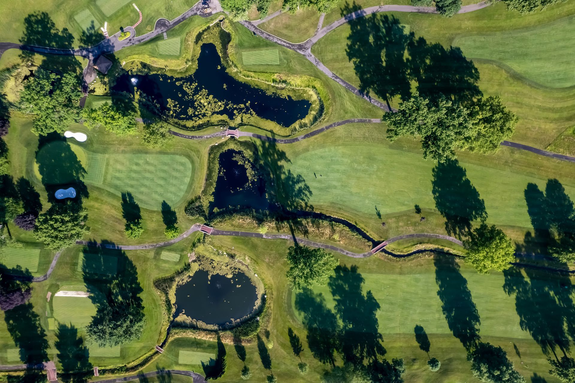 Aerial view of a golf course with ponds, green fairways, and trees casting long shadows on a sunny day.