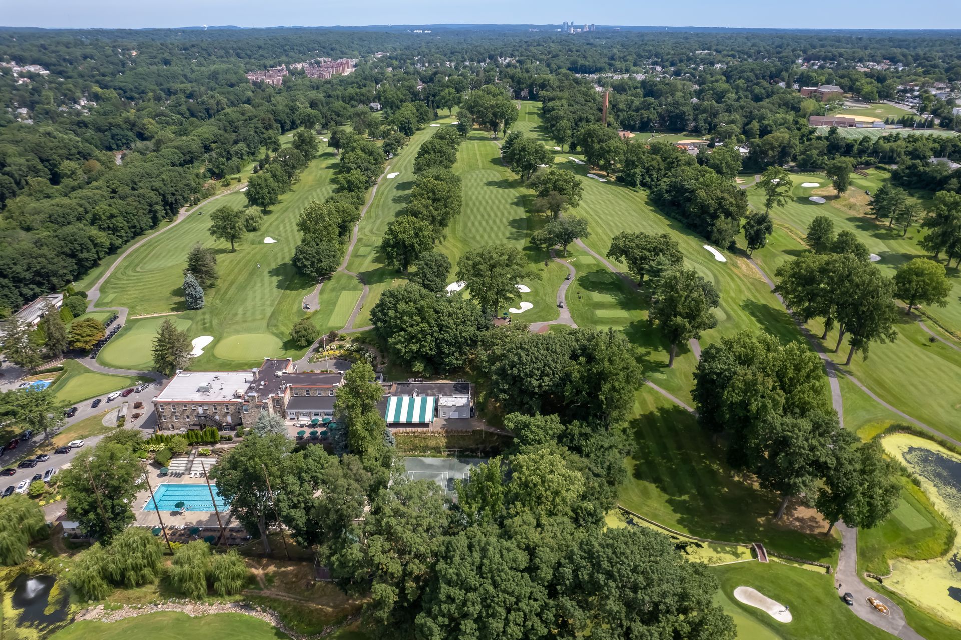 Aerial view of a green golf course with trees, fairways, a clubhouse, and a blue swimming pool.