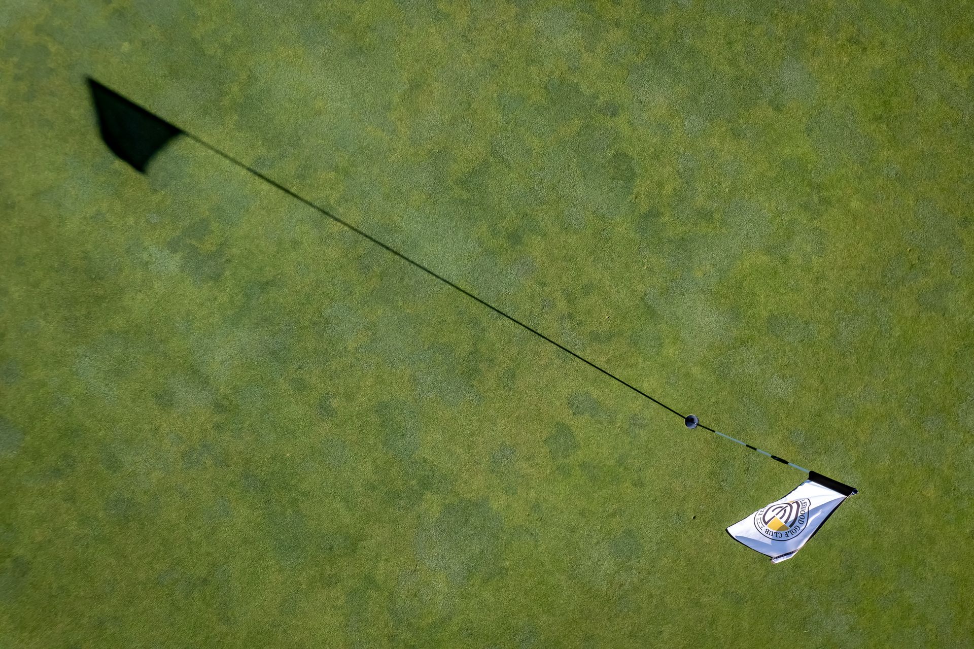 Shadow of a golf flag extending across green grass, suggesting a sunny day on a course.