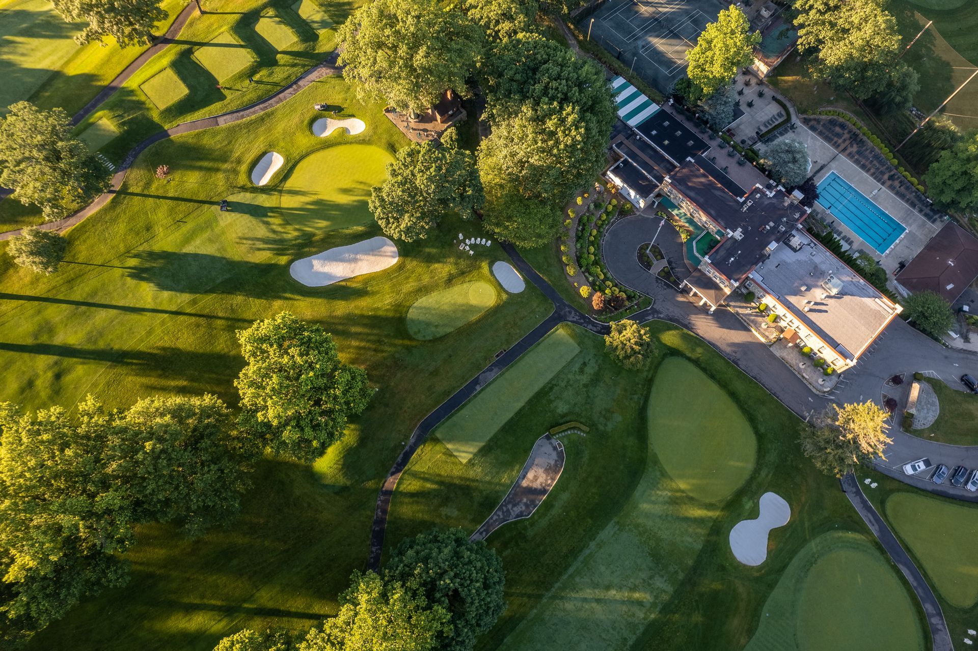 Aerial view of a green golf course with sand traps and a clubhouse with a pool.