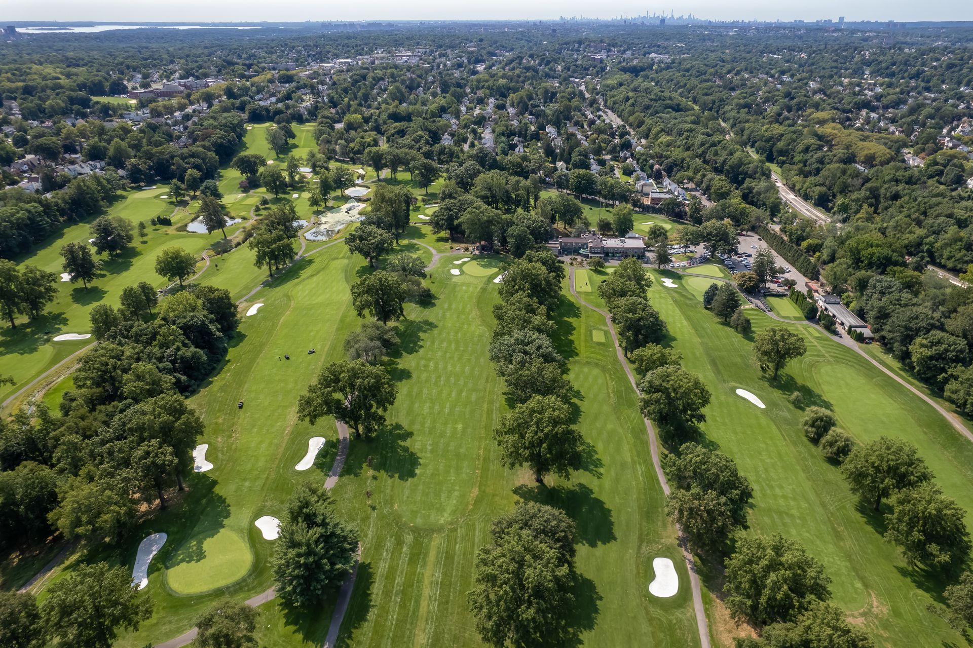 Aerial view of a green golf course with rows of trees, white sand traps, and a clubhouse.
