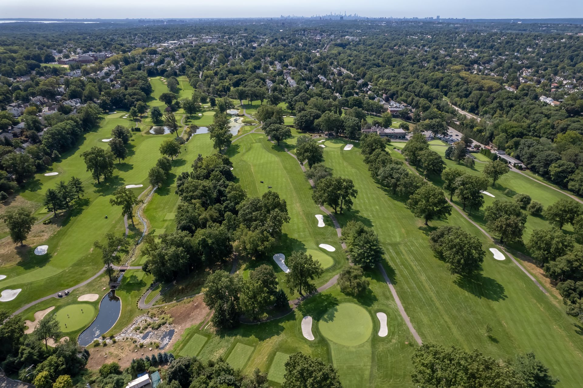 Aerial view of a green golf course with fairways, trees, bunkers, and several visible white golf flags.