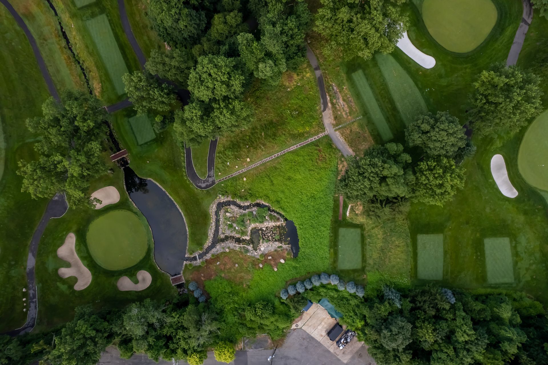 Aerial view of a golf course with green fairways, sand traps, and water features surrounded by trees.